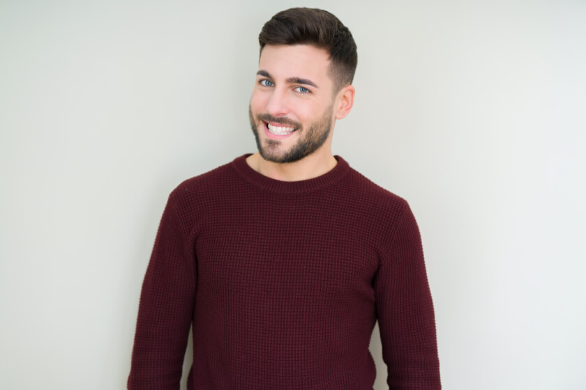 Man smiling in maroon sweater against neutral background.