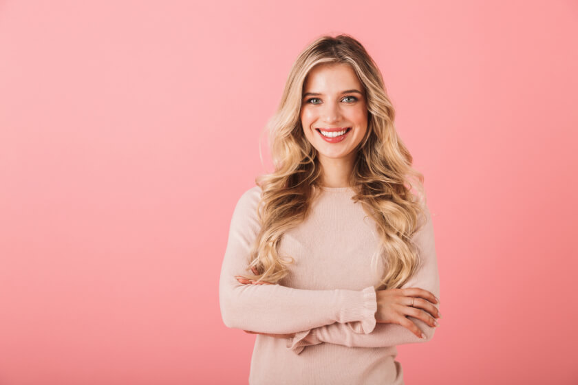 Woman smiling with arms crossed on pink background.