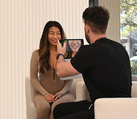 Man photographing smiling woman with tablet indoors.