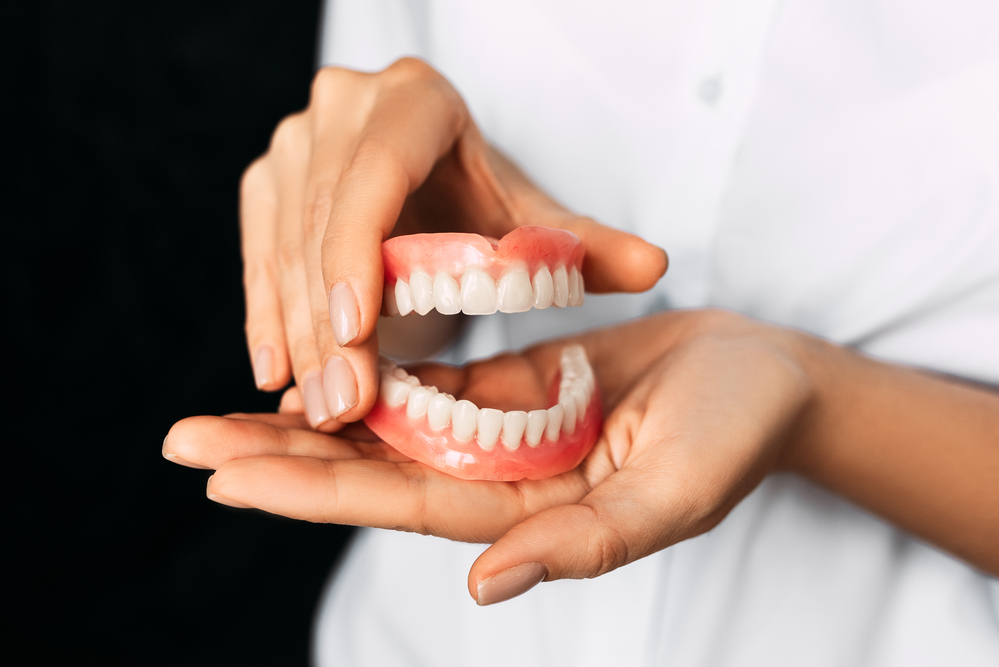 Hands holding upper and lower dentures.